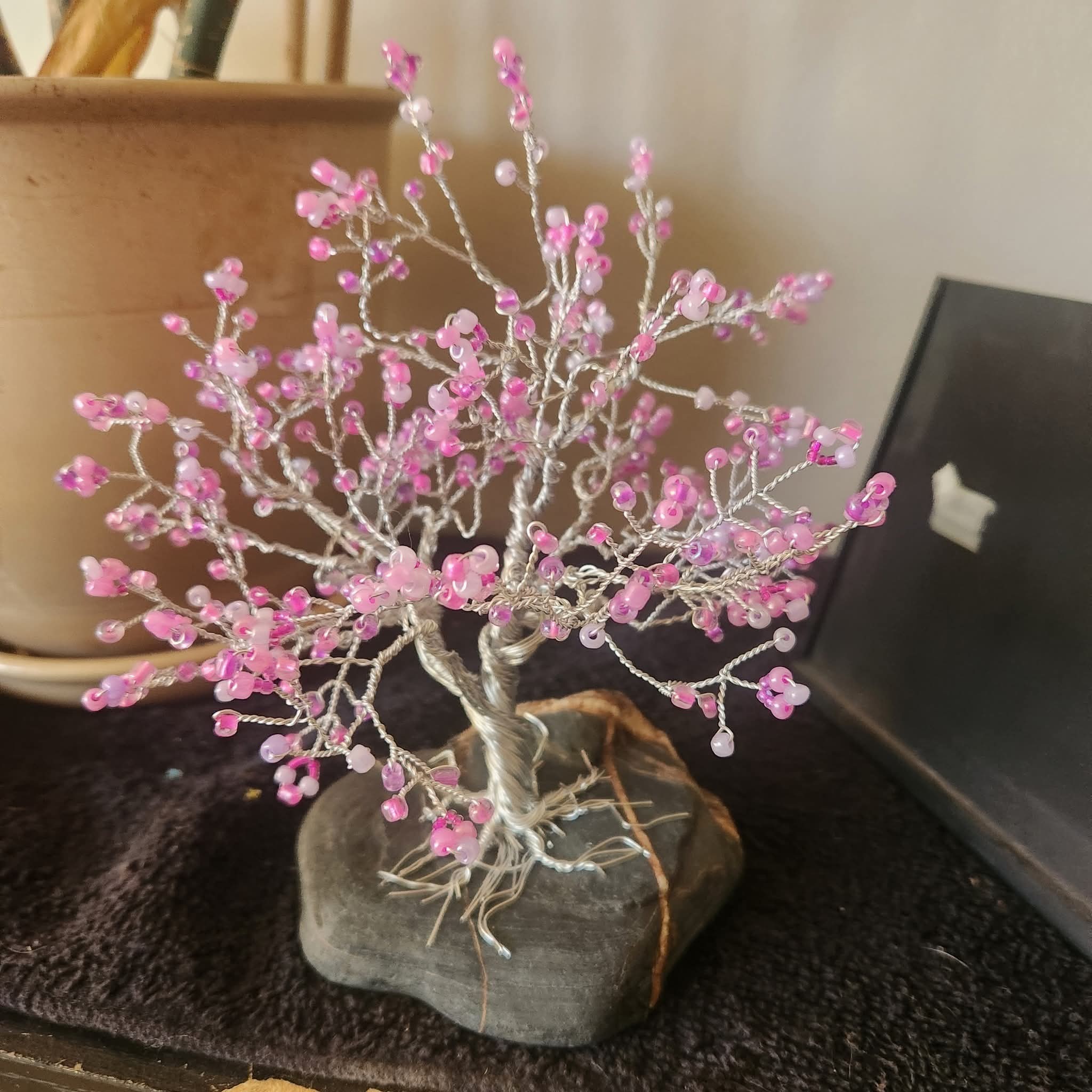 Blossoms of Becoming is a one-of-a-kind, handmade twisted wire tree adorned with soft pink glass beads and rooted in a unique natural river rock with quartz veins. This piece symbolizes gentle growth, transformation, and the beauty of evolving in your own time.